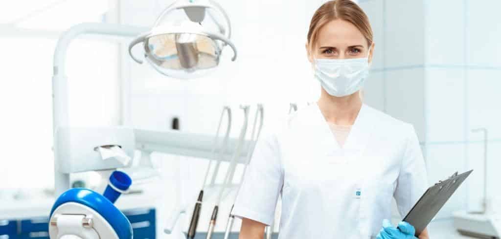 Osoba z zespołu stomatologicznego trzymająca podkładkę z dokumentacją w gabinecie