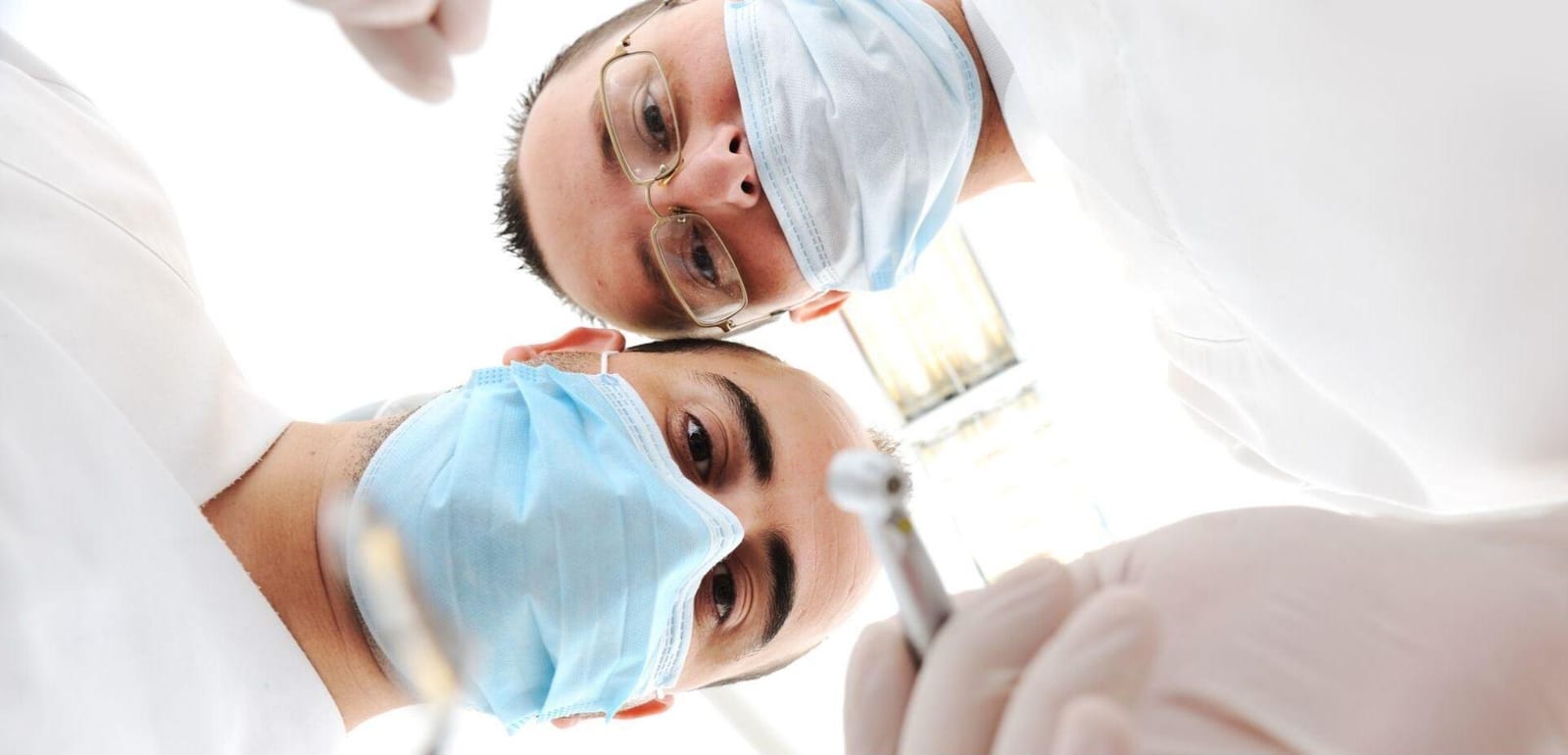 Dwie osoby z zespołu stomatologicznego w maseczkach, widziane z pozycji pacjenta