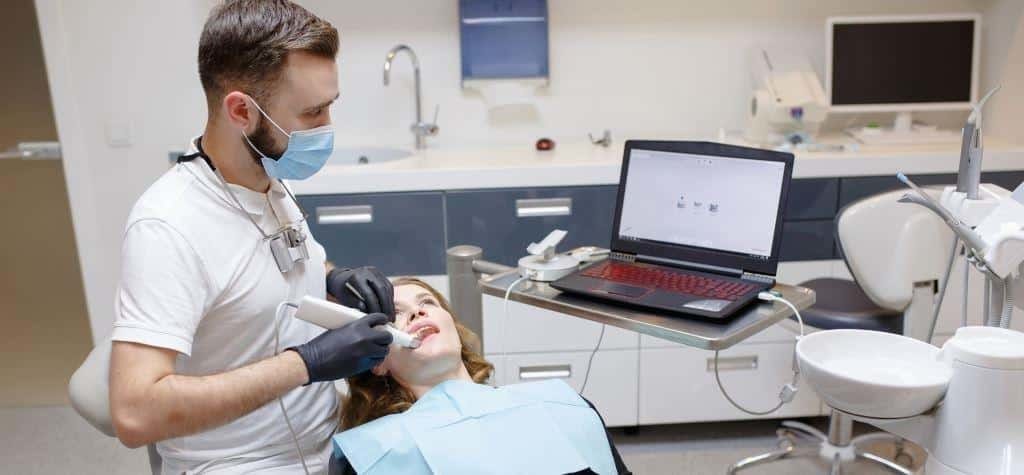 Dentysta używający ręcznego skanera obok pacjenta i laptopa