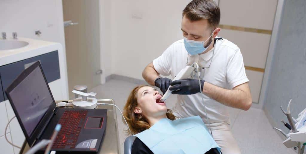Dentysta leczący pacjenta obok laptopa