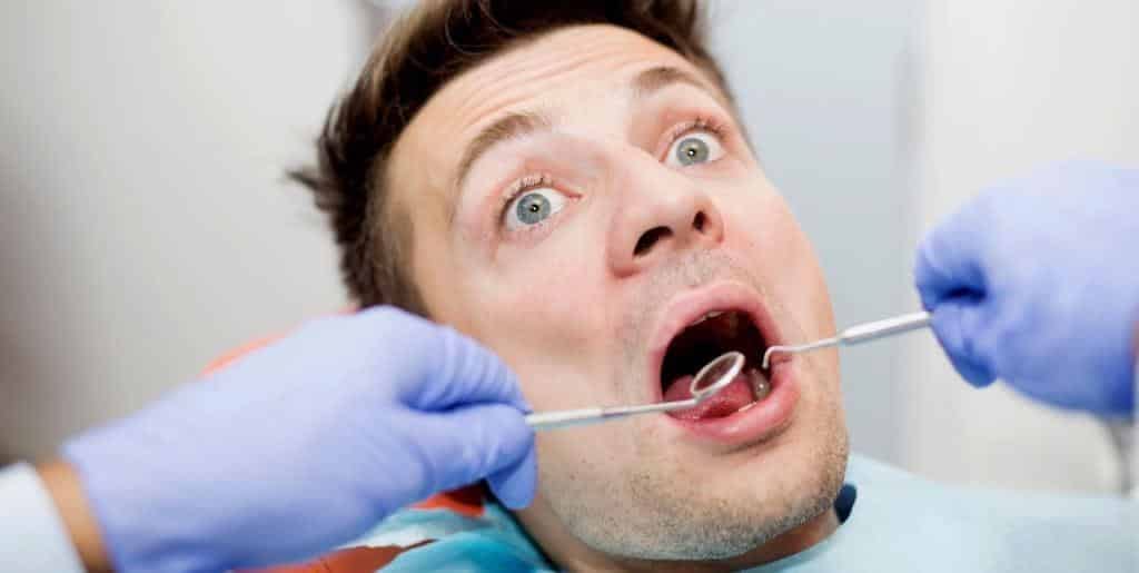 Pacjent z otwartymi ustami podczas badania lusterkiem przez dentystę