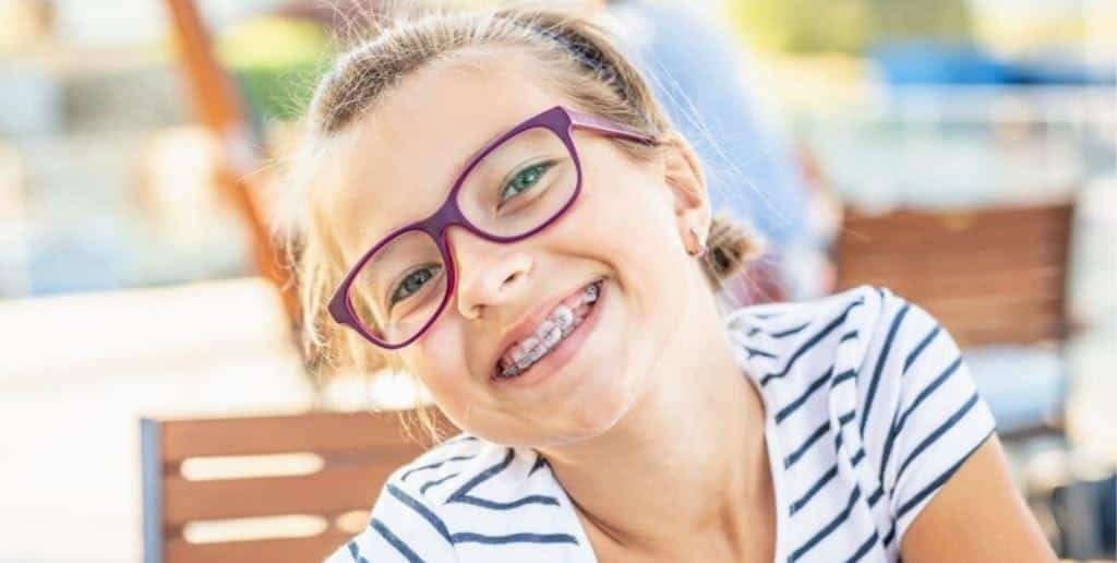 Uśmiechnięte dziecko w okularach i stałym aparacie ortodontycznym