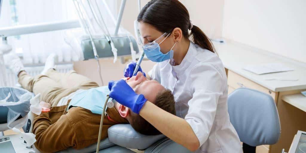 Osoba z zespołu stomatologicznego bada pacjenta w fotelu