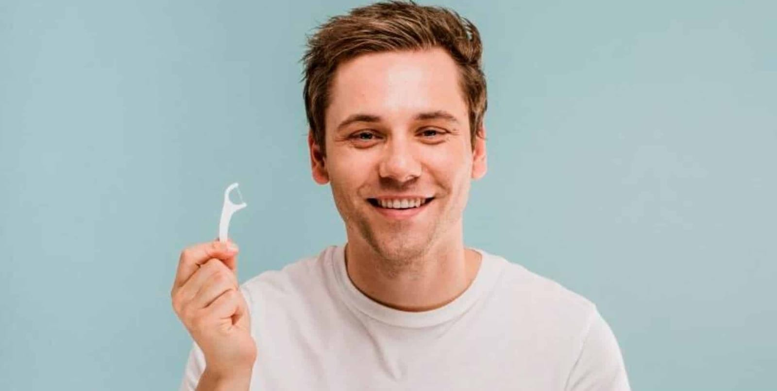 Uśmiechnięty mężczyzna trzyma uchwyt z nicią dentystyczną