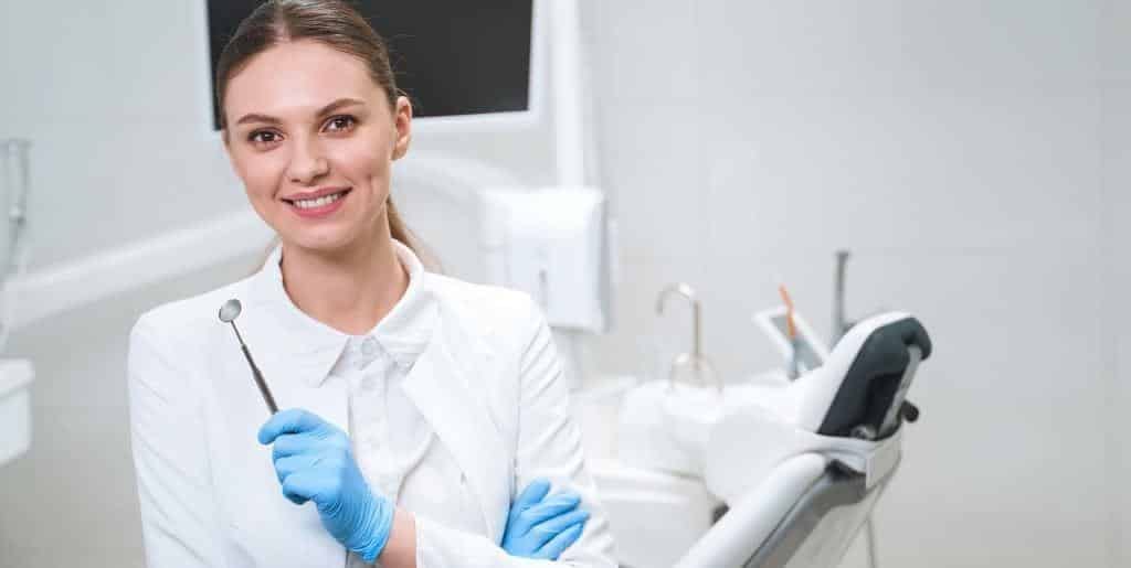 Pracownik gabinetu trzymający lusterko obok fotela dentystycznego