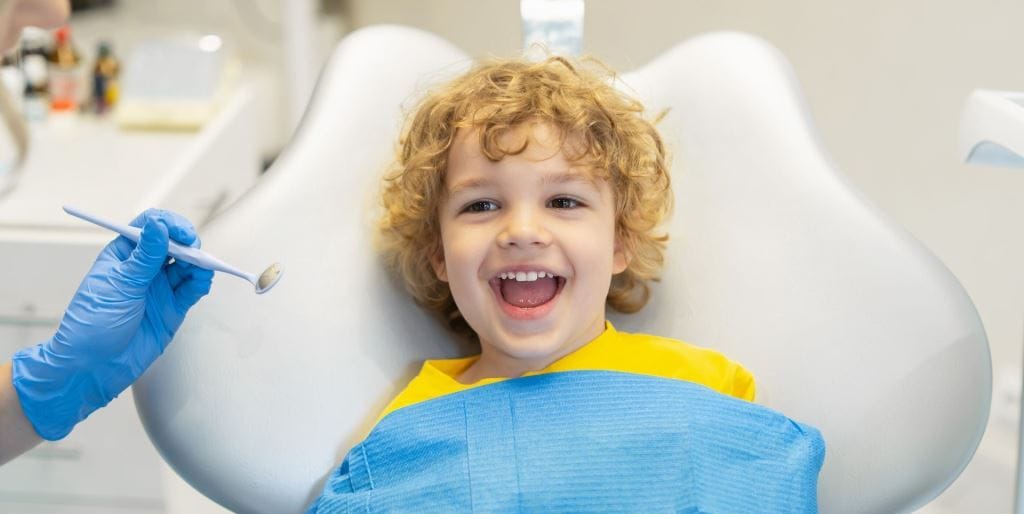Dziecko uśmiechające się na fotelu obok lusterka dentystycznego