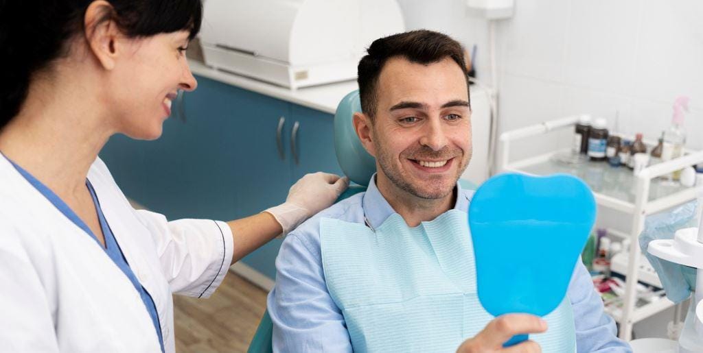 Pacjent trzyma niebieskie lusterko obok członka zespołu dentystycznego