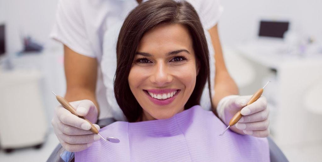 Pacjentka w fioletowym śliniaku, obok dentysta trzymający narzędzia