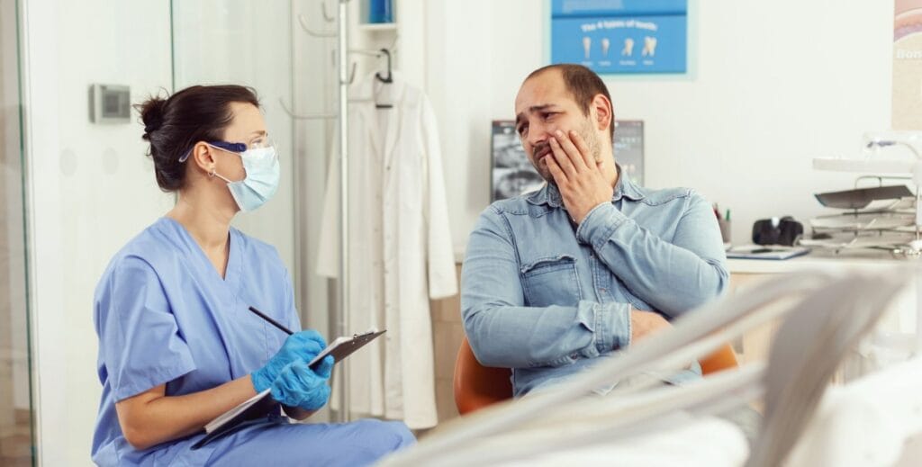 Dentysta rozmawiający z pacjentem trzymającym się za policzek