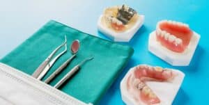 Imaginea prezintă un set de instrumente dentare și modele de maxilare ale pacienților pe un fundal albastru. Pe fundalul verde se află instrumente dentare precum forcepsul și sondele. Alături sunt vizibile modele ale dentiției în diferite stări, inclusiv pete și carii. Imaginea are un fundal albastru.