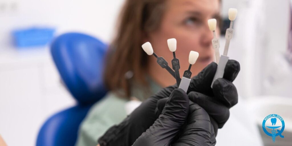 The photograph shows the hand of a person wearing black gloves, holding various dental instruments with white tips. In the background, the blurred face of a person sitting in a dental chair can be seen. The image focuses on the representation of the tools used by the dentists during the procedure.