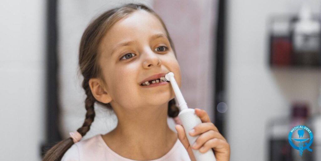 Усмихнато момиче с косички си мие зъбите с електрическа четка за зъби, като се виждат млечните му зъби, тъй като зъбният му апарат се подменя.