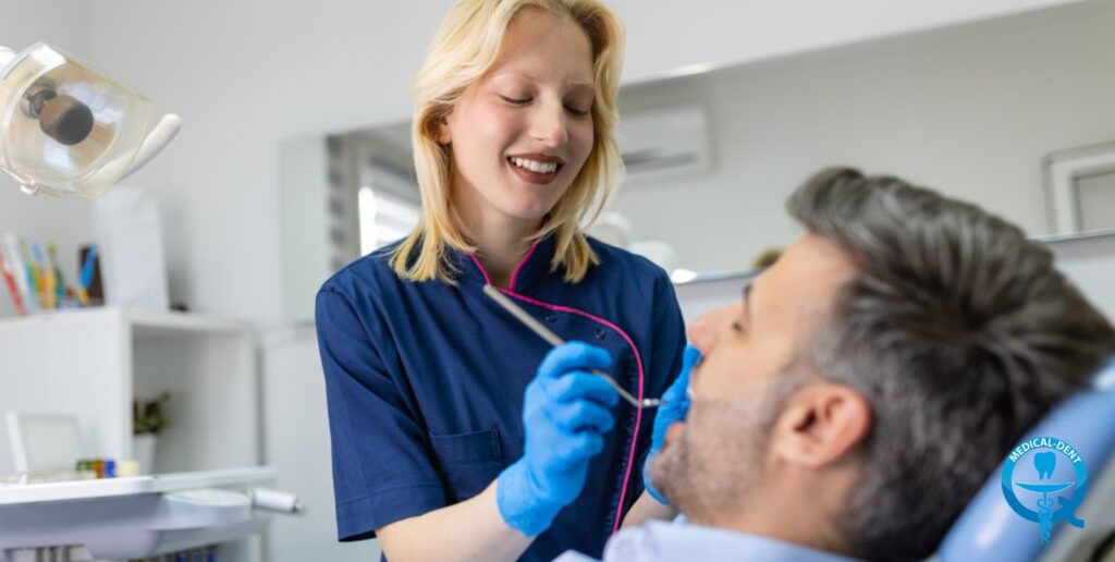 Uśmiechnięta dentystka w granatowym fartuchu i niebieskich rękawiczkach przeprowadza badanie jamy ustnej pacjenta leżącego na fotelu dentystycznym w jasnym gabinecie stomatologicznym w Wielkiej Brytanii.