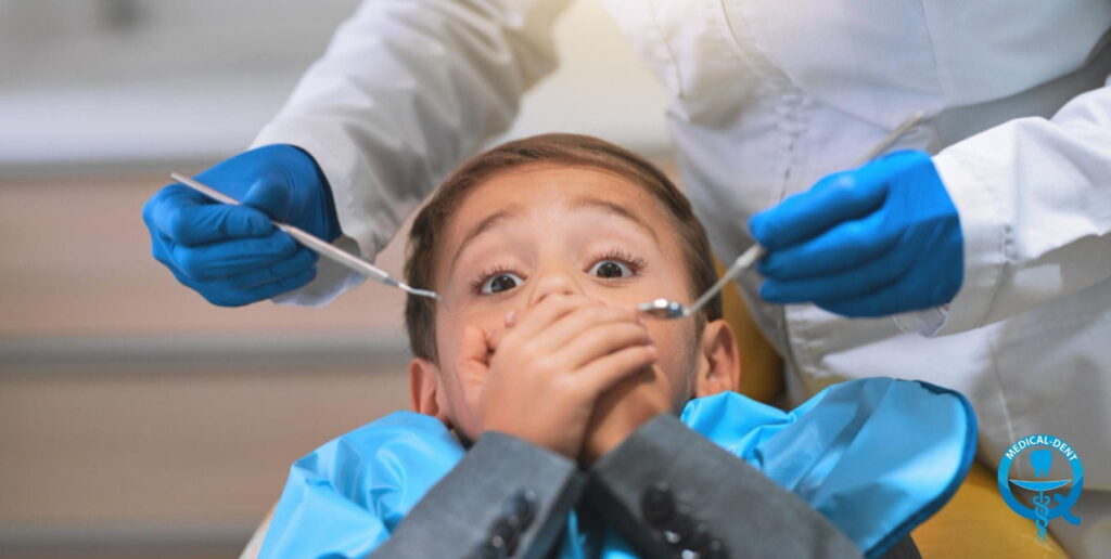 Przestraszone dziecko zakrywające usta dłońmi podczas wizyty u dentysty, w tle dentysta w niebieskich rękawiczkach trzymający narzędzia stomatologiczne
